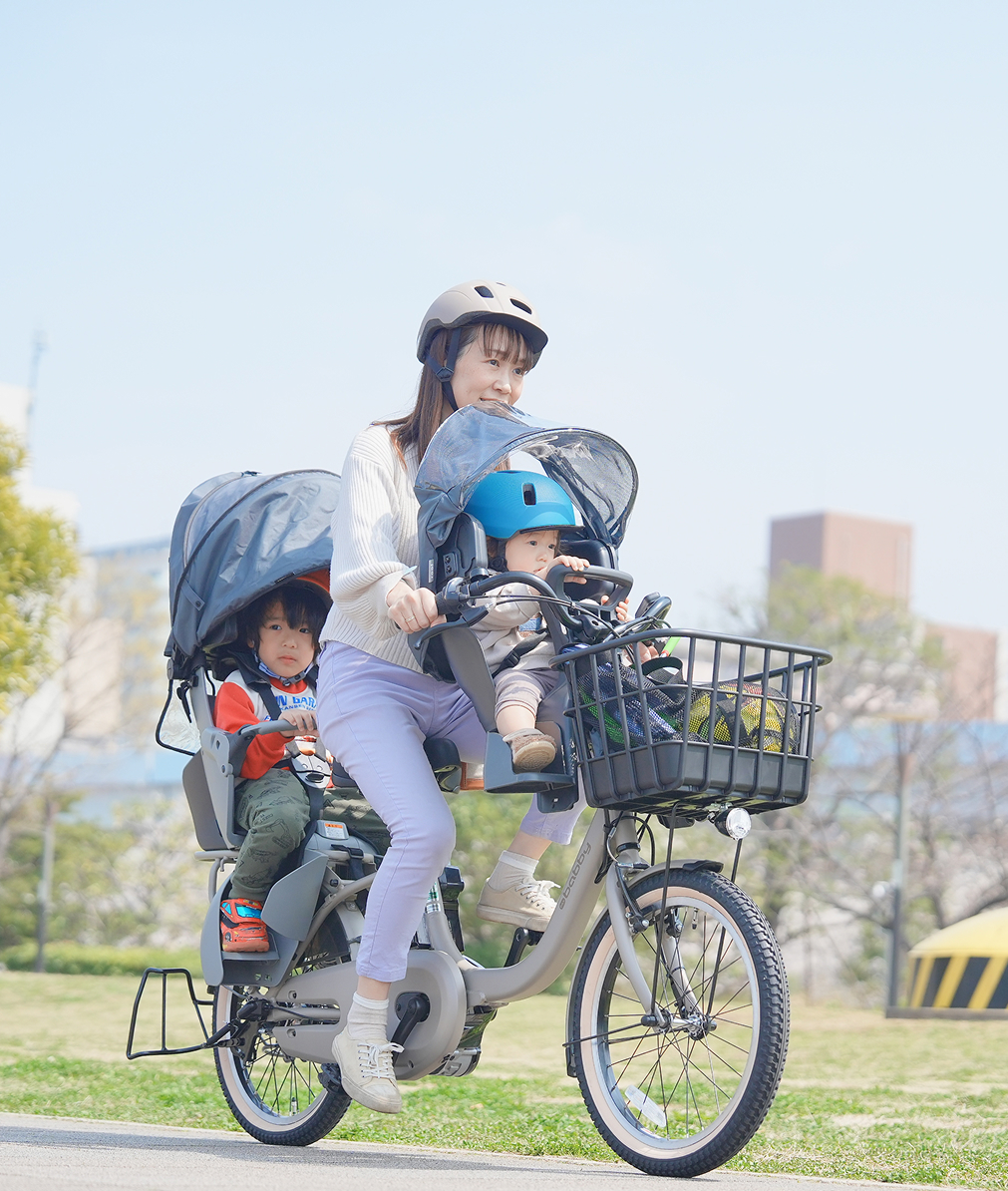 子供を自転車の後ろに乗せて歩いている母親