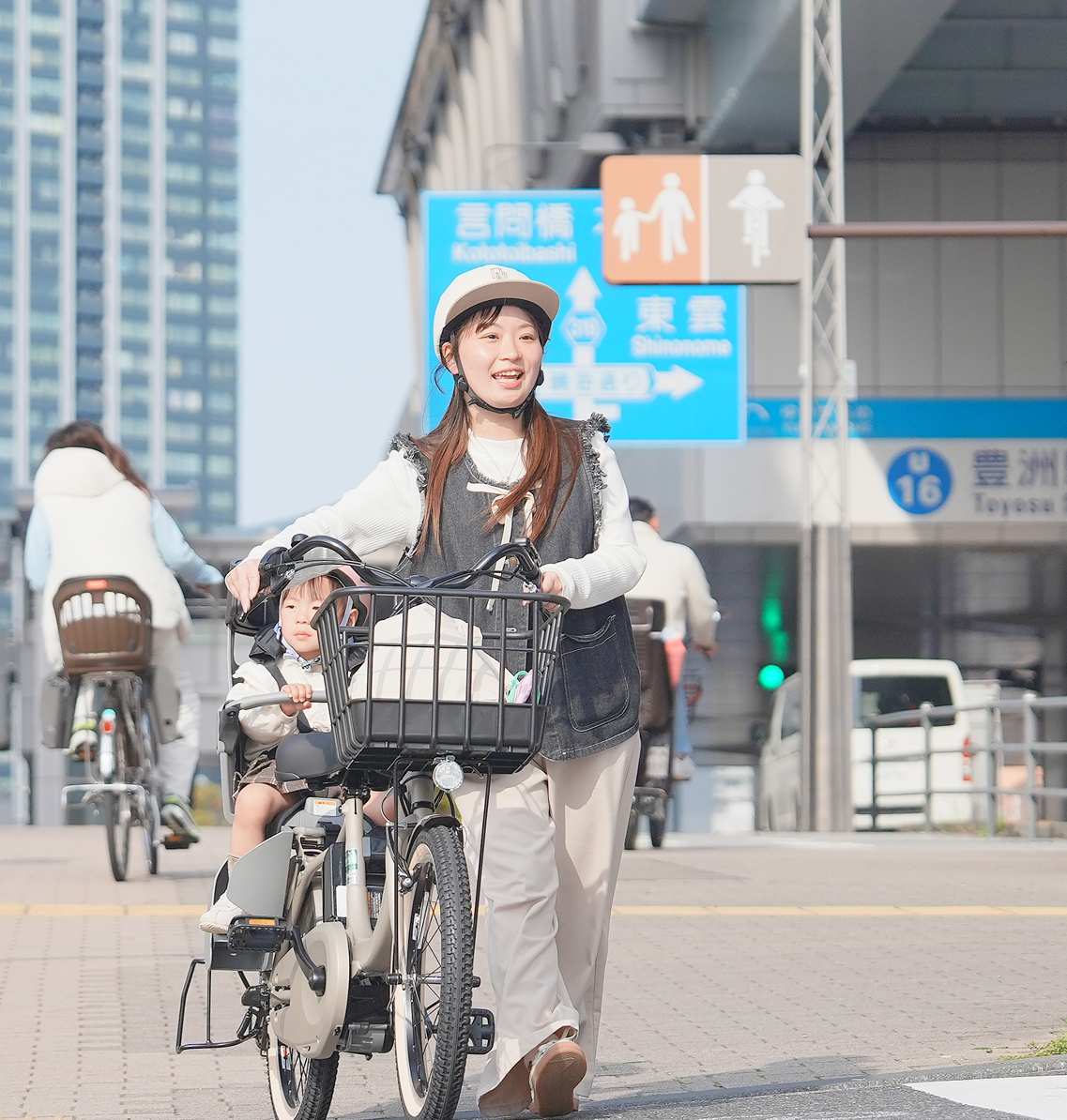 子供を自転車の後ろに乗せて歩いている母親